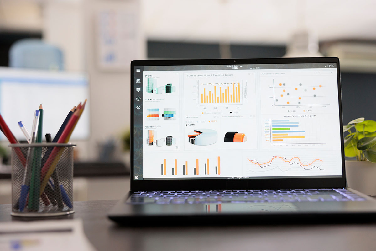 Laptop showing a business analytics dashboard with bar charts and scatter plots on a desk beside a pencil holder in an empty office